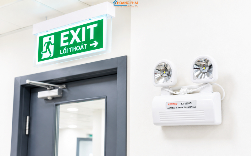 Ảnh chụp cận cảnh đèn exit hai mặt treo trên cửa và đèn sự cố hai chóa gắn tường hành lang